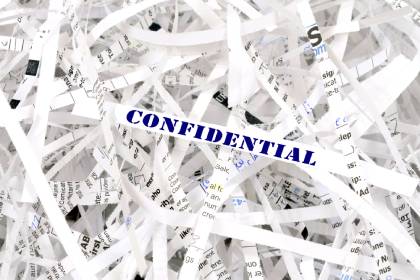 A pile of shredded paper documents with bits of illegible writing on them. The piece on top says confidential.