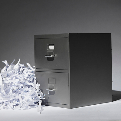 A filing cabinet situated in an open space with a pile of shredded paper documents sitting next to it.