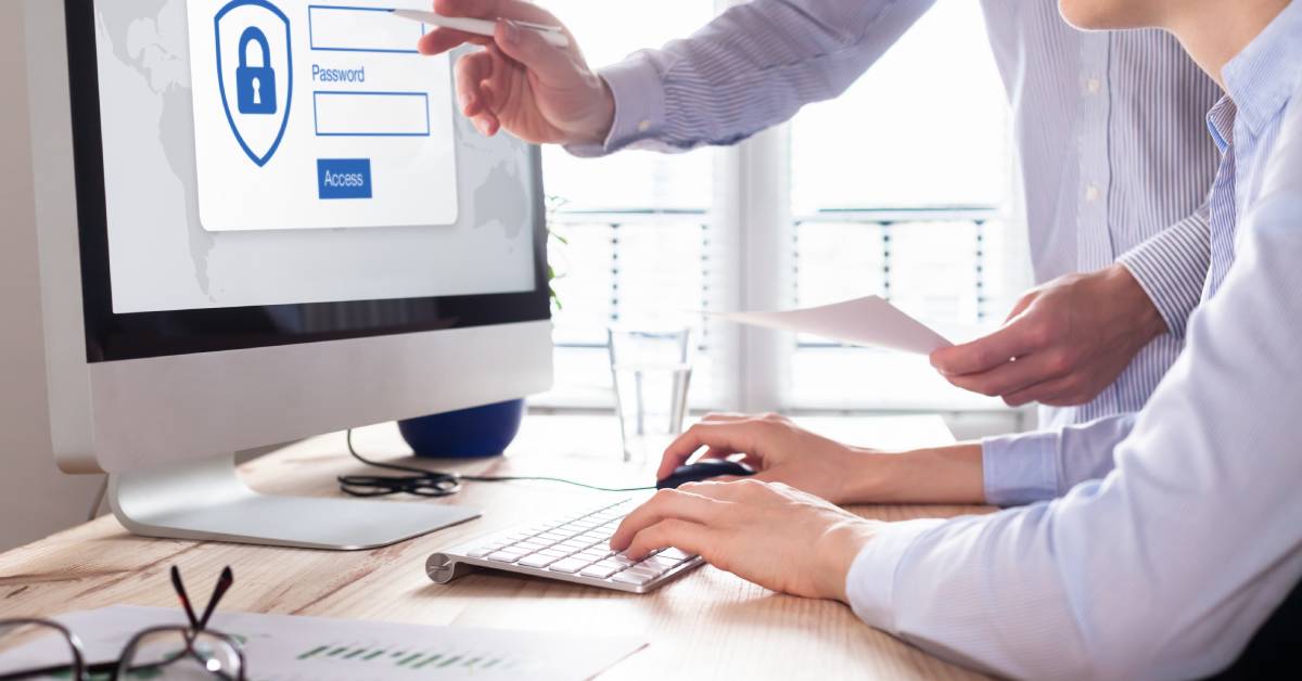 Two people in a business setting sitting in front of a desk using a computer with a security login on the screen.