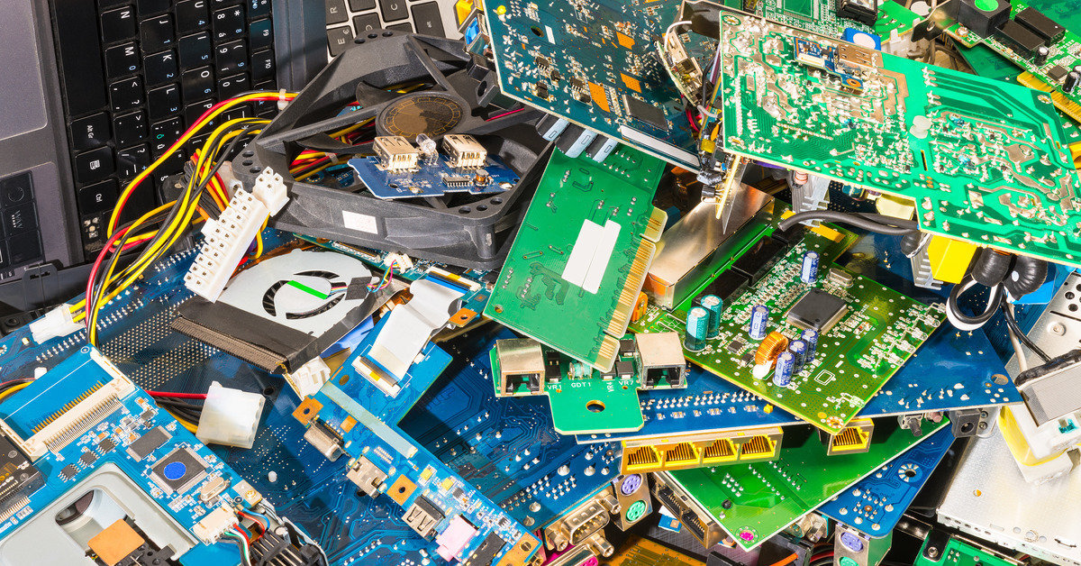 A pile of discarded electronics equipment including motherboards, keyboards, and fans contributing to e-waste.