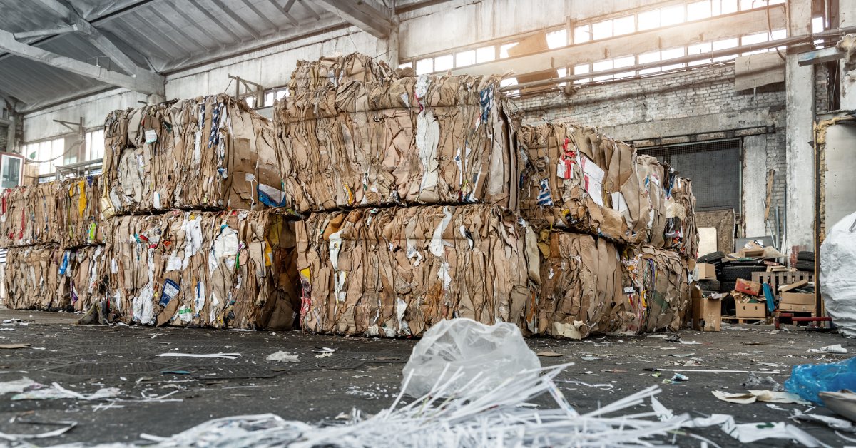 An industrial warehouse with large bales of cardboard stacked together behind the remains of shredded documents.