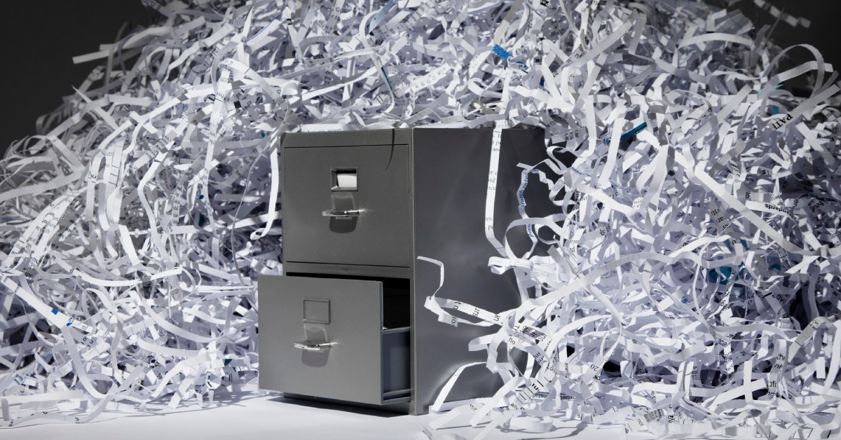 The shredded remains of paper documents piled on top of a metal filing cabinet over a black background.