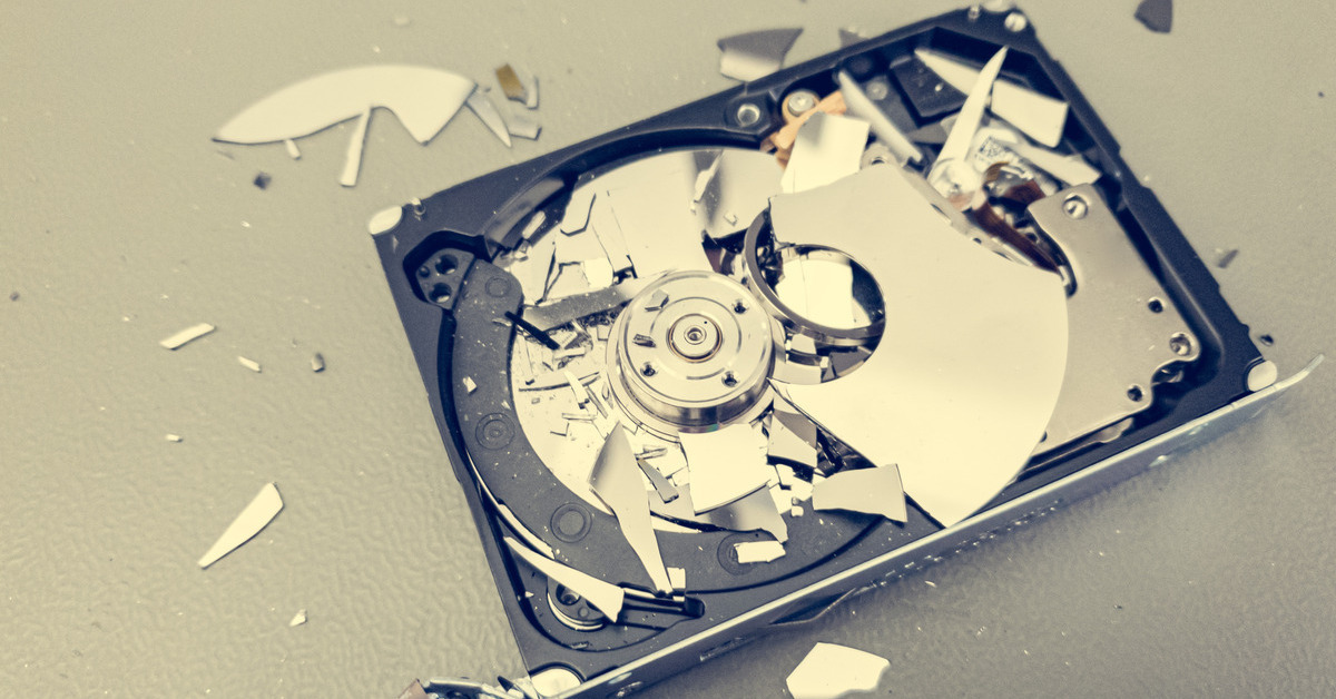 A broken hard drive sitting on a table with the tape exposed. There are small pieces of a disc scattered around.