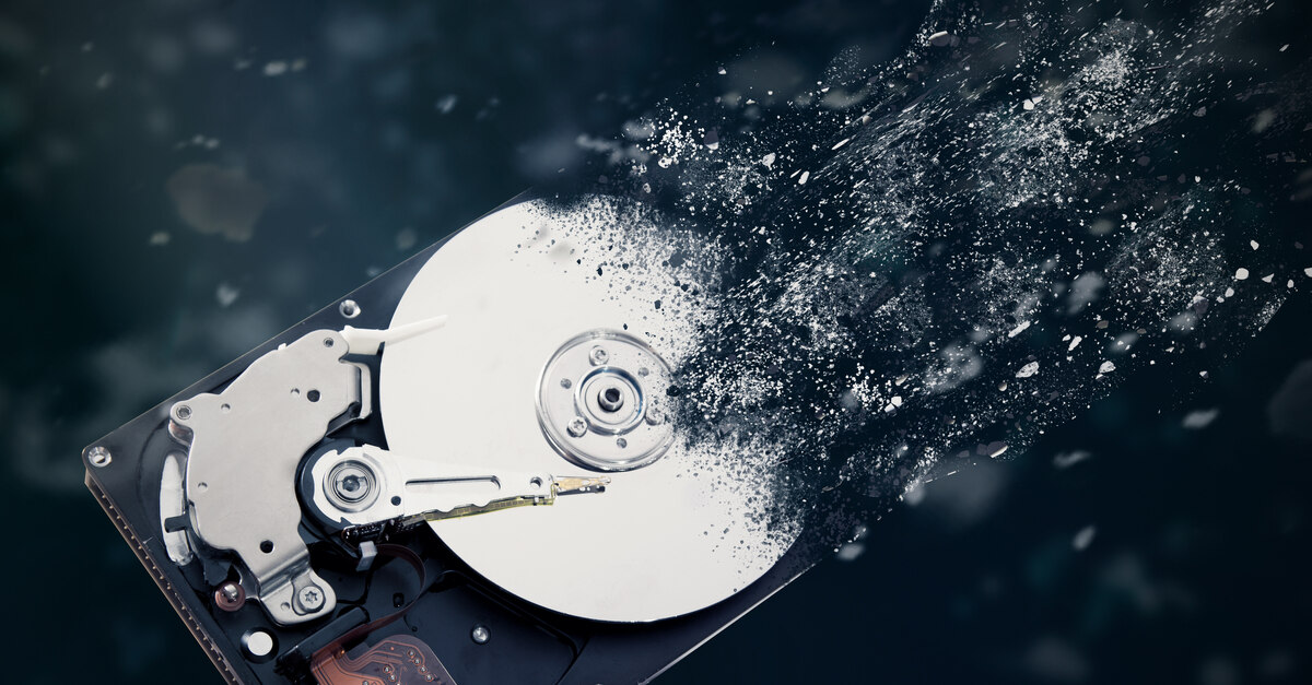 A physical hard drive depicted dissolving and turning into small pieces of dust over a black background.