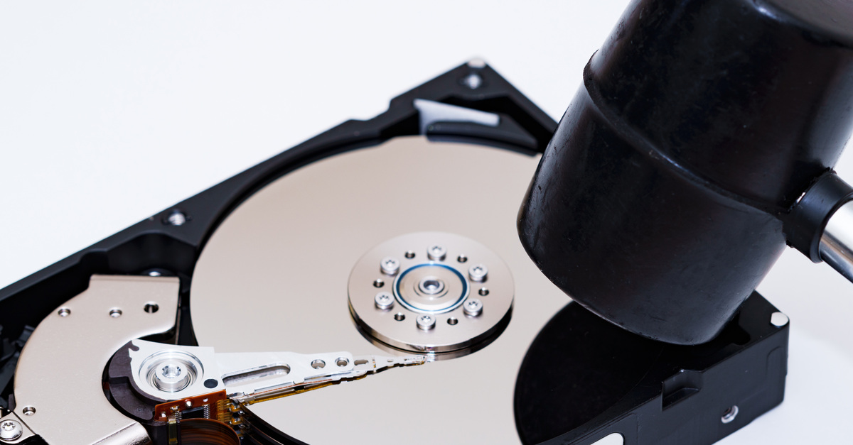 A mallet with a black top and metal handle ready to smash a physical hard drive in front of a white background.