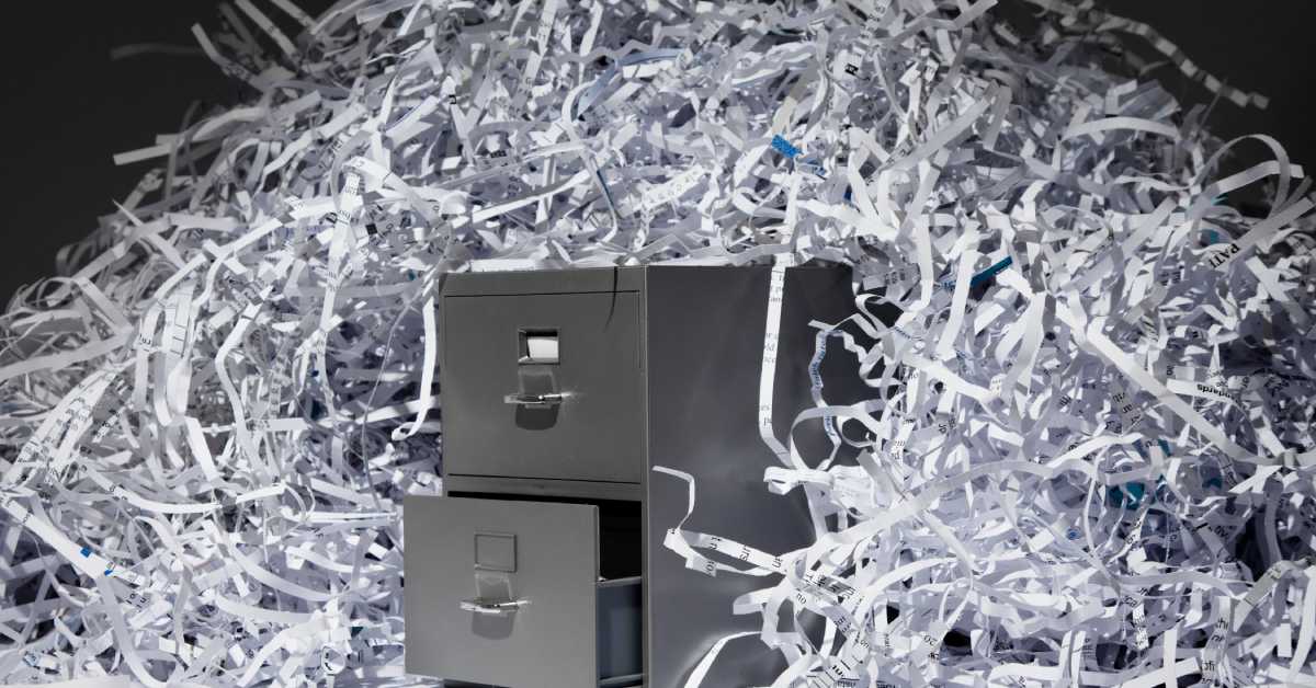 A filing cabinet with the bottom drawer slightly open and a pile of shredded document remains lying on top of it.