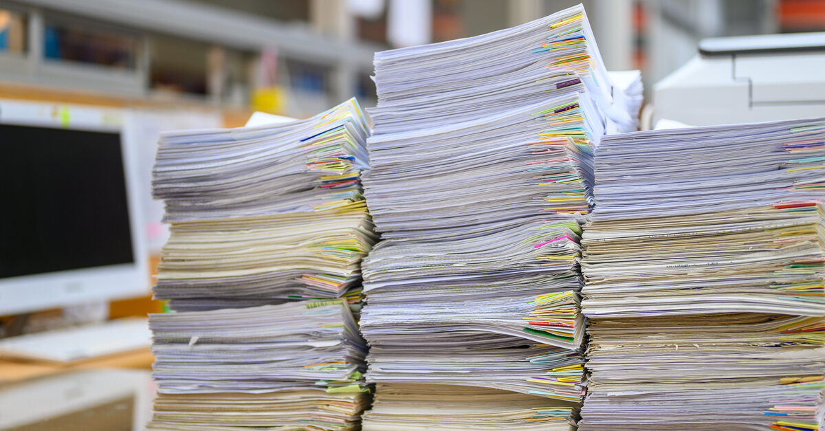 A stack of documents with colored labels attached to them on a desk in an office. There's a computer turned off in the background.