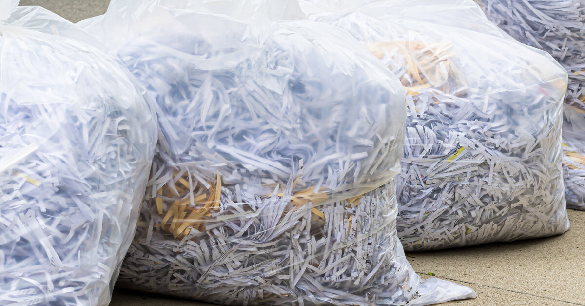 A row of see through trash bags with shredded documents inside of them sitting outside on the sidewalk.