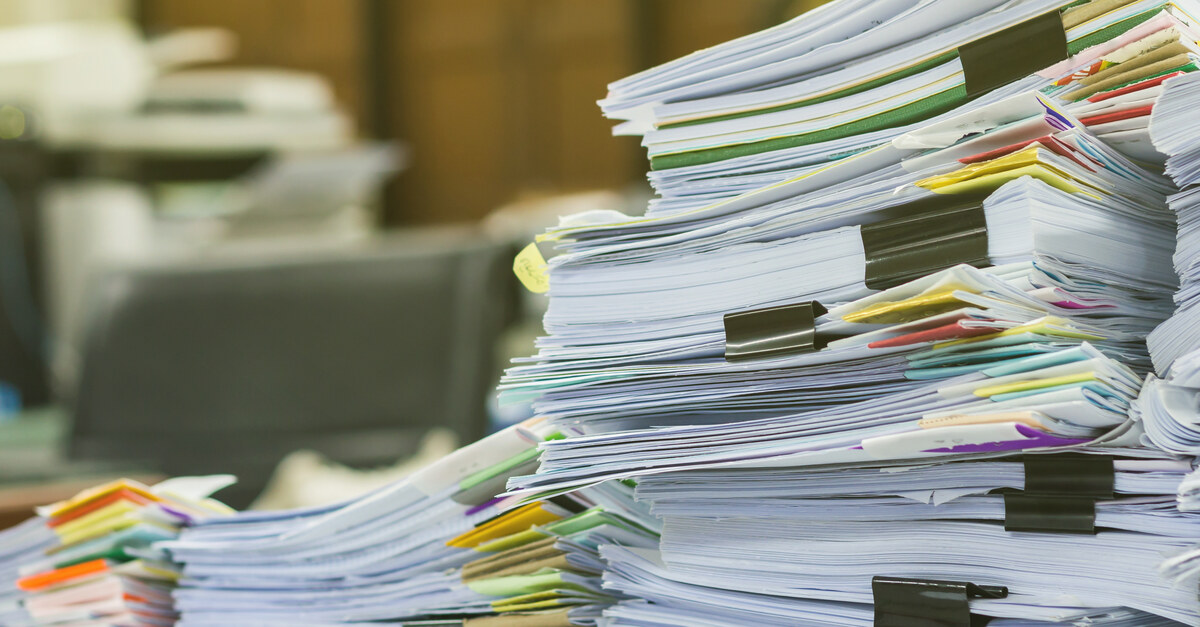 Piles of professional documents sitting on a desk in an office with colored stickers for organization.