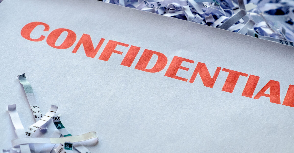 A pile of shredded documents in front of a dark background with a large piece of paper sitting on top that says CONFIDENTIAL.