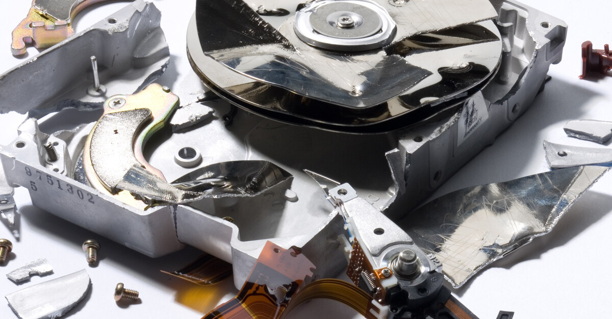 A destroyed hard drive with various small pieces surrounding it. It sits against a white background.
