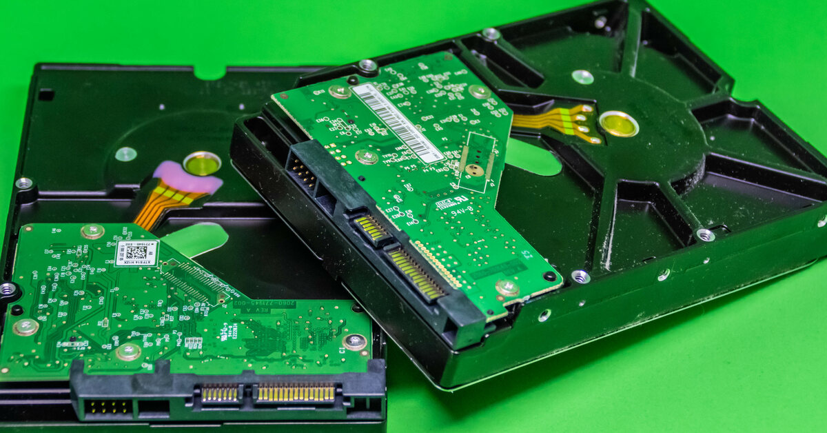 Two hard drives with cables and circuits attached to them sitting against a green background partially on top of each other.