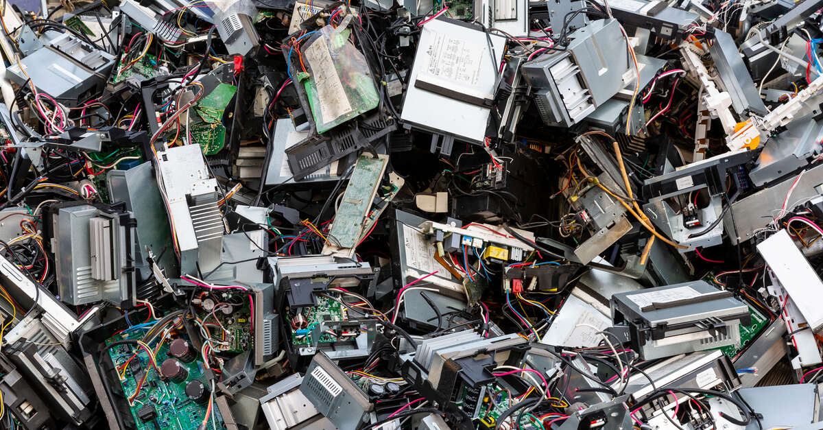 A large pile of e-waste almost completely fills the frame. It's composed of old computers, drives, and other equipment.