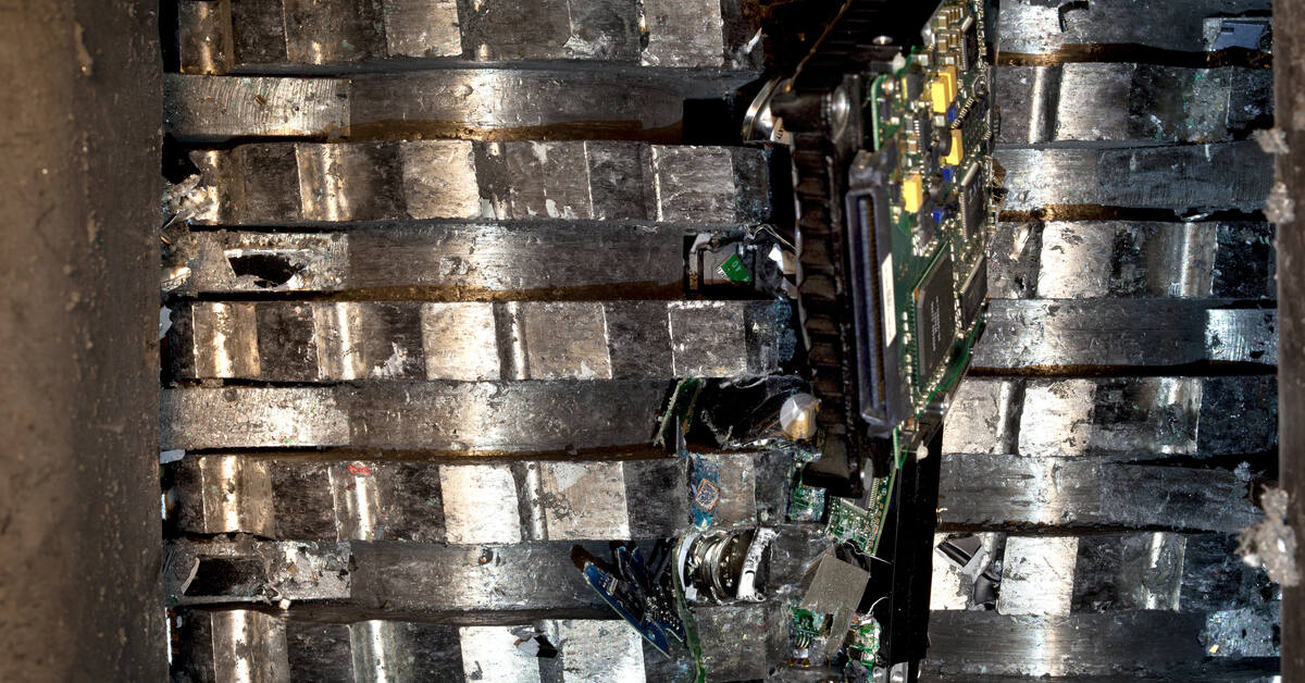 A metal grinder for crushing electronic components with pieces of a destroyed hard drive inside of it.