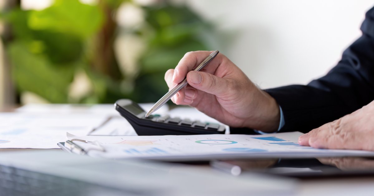 A person sitting at a desk in an office writes on a clipboard. They have a calculator and other papers next to them.