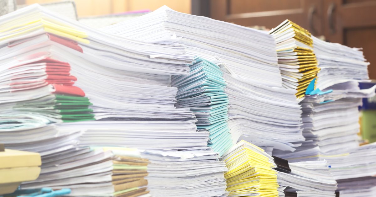 Large stacks of color-coded financial documents sit on top of one another on a desk, ready for disposal.