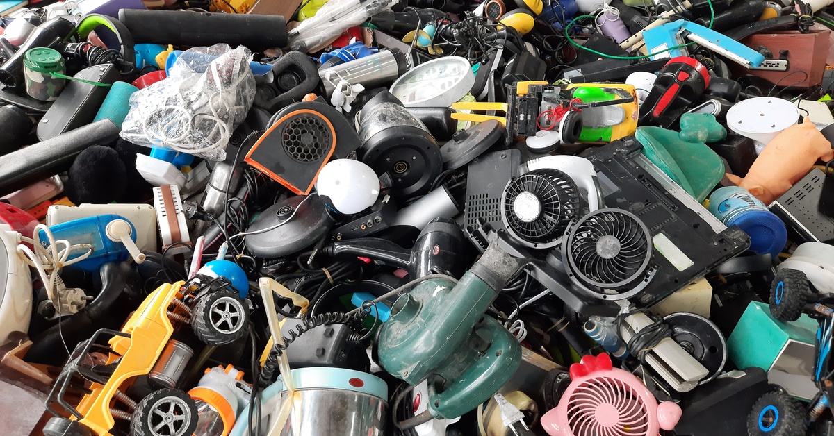 A pile of old household products, including toys, electronic waste, and handheld fans fills the frame.