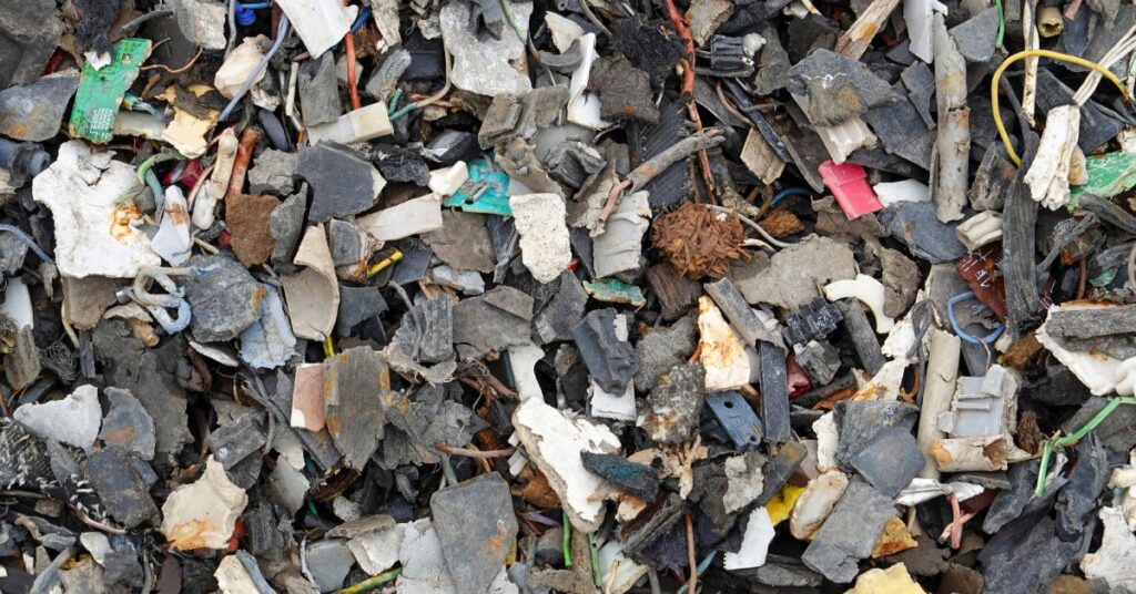 A close-up of a pile of broken pieces of metal and plastic from destroyed electronic devices at a scrapyard.