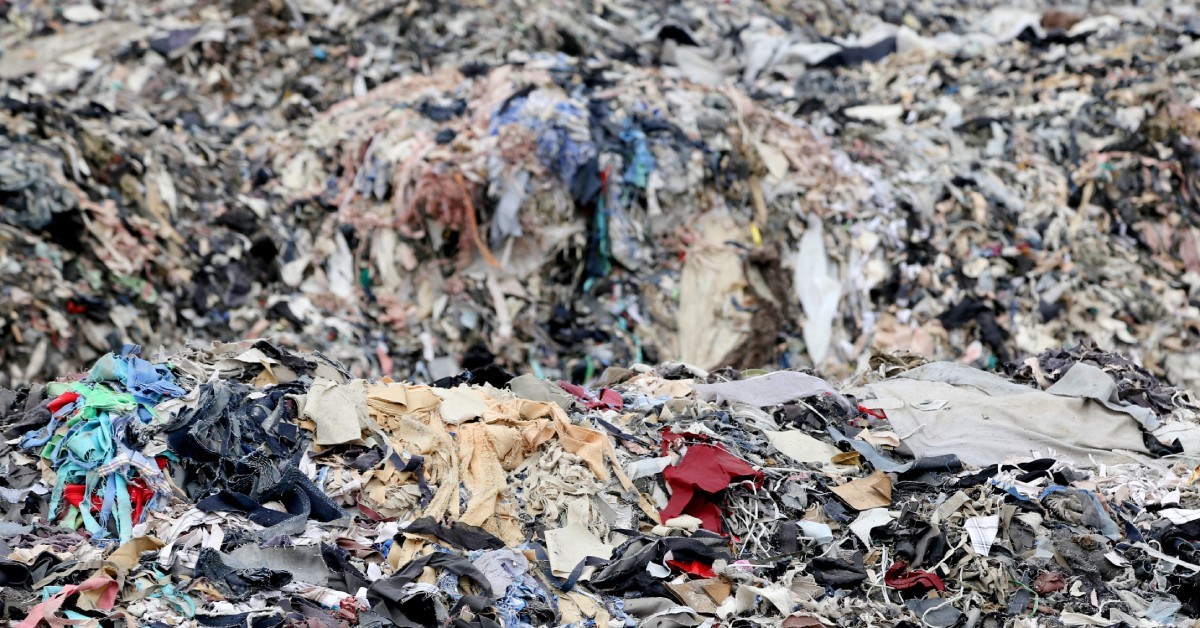 Piles of old textile waste sitting outdoors in a dump decomposing in the open air adding to carbon emissions.