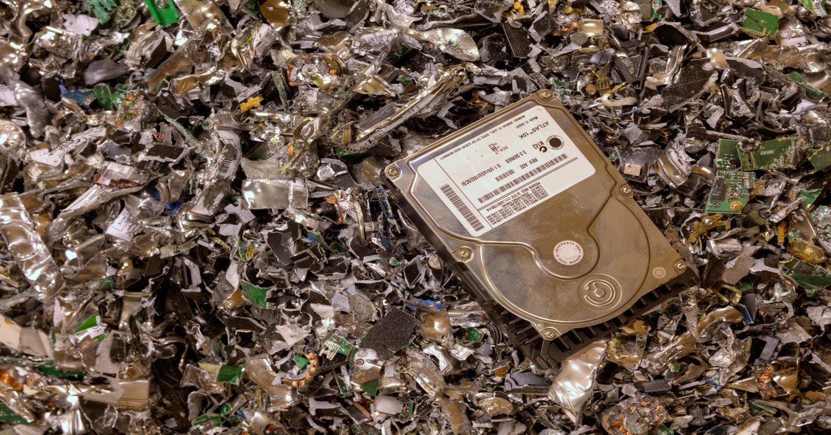 An intact hard drive laying on top of a pile of other drives that have already been shredded by a machine for security.