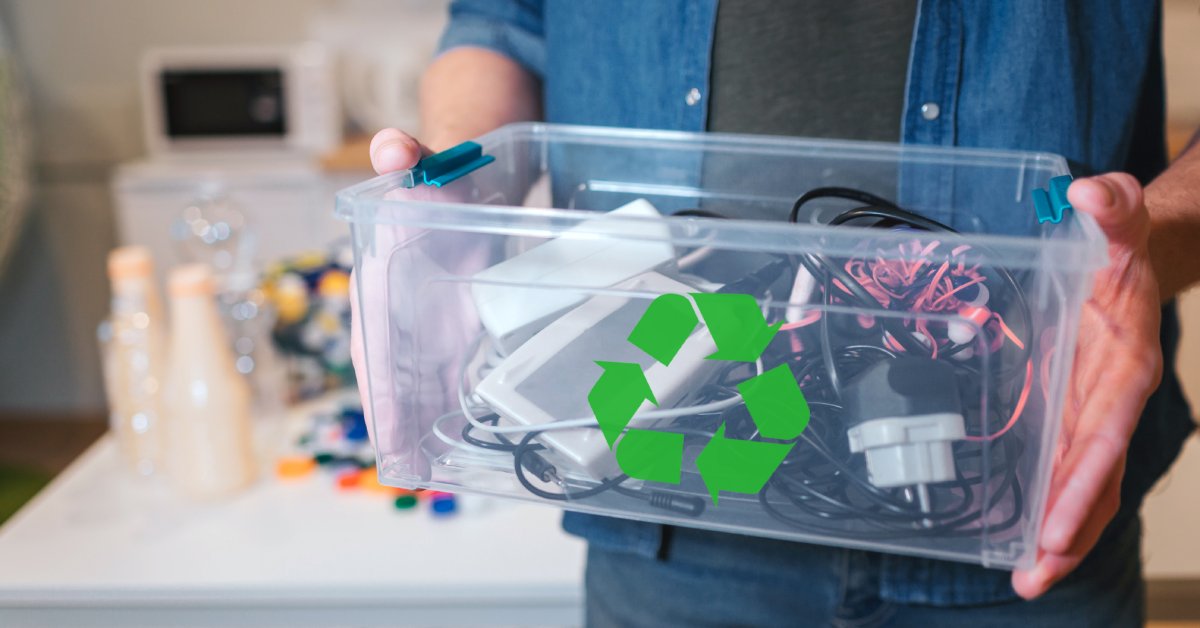 A person holding a small plastic bin with a recycling symbol on it. The bin is transparent and full of electronics.