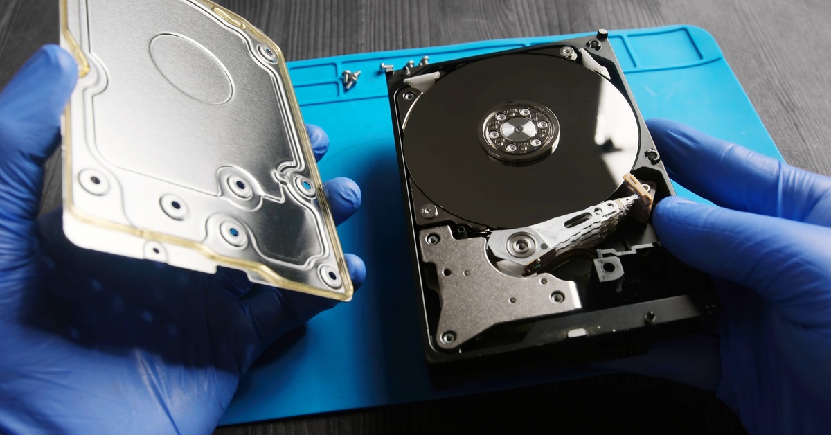 Two gloved hands, each holding a side of a computer hard drive. One holds the drive and the other holds the case.