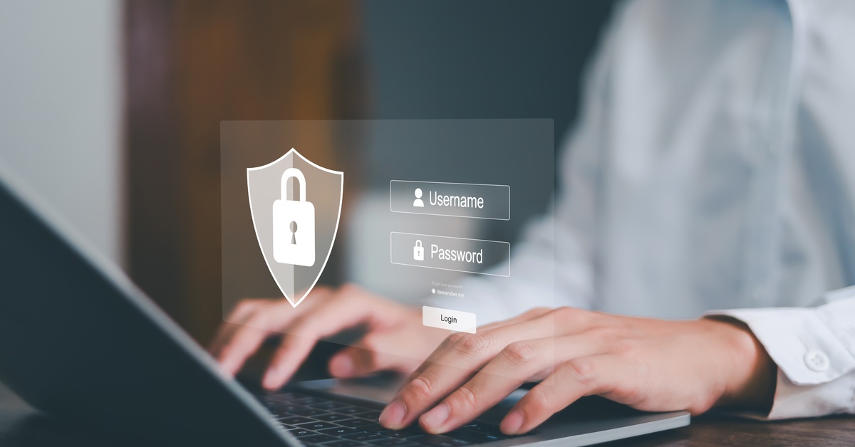 A person using their laptop. A graphic above their hands shows a lock, shield, and fields for username and password.