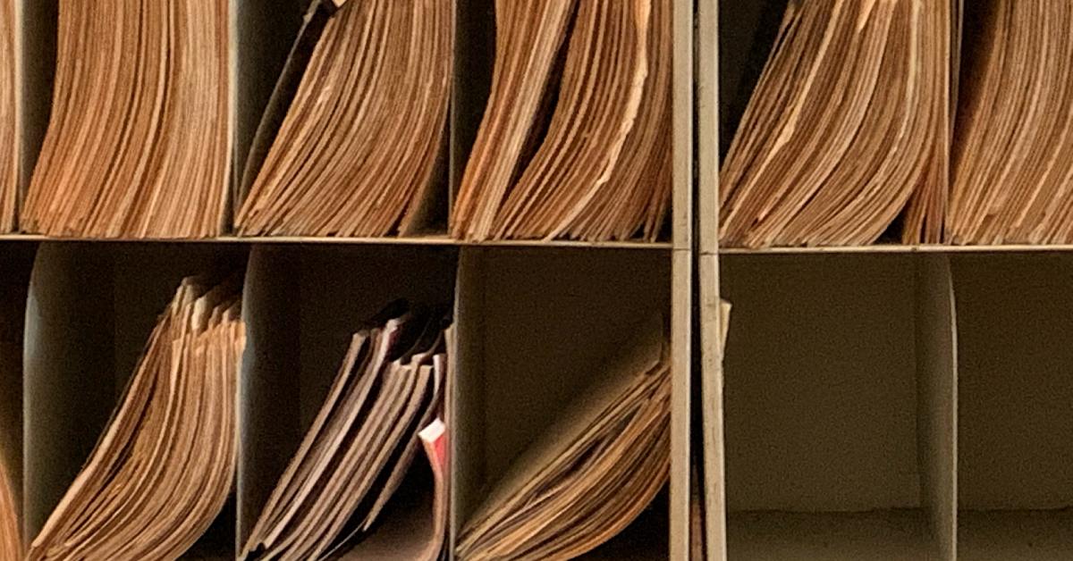 A pair of metal shelves with several narrow compartments. Most compartments hold aged manila folders.