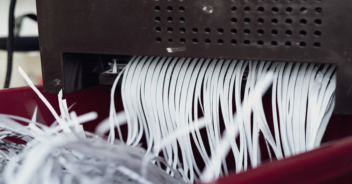 A close-up on the output area of an industrial shredder that is in the process of shredding documents into strips.
