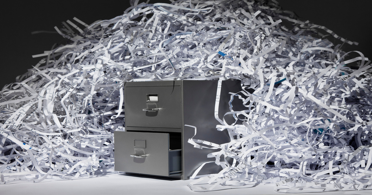 A large pile of shredded paper strips draped over the sides of a small metal filing cabinet with one drawer open.
