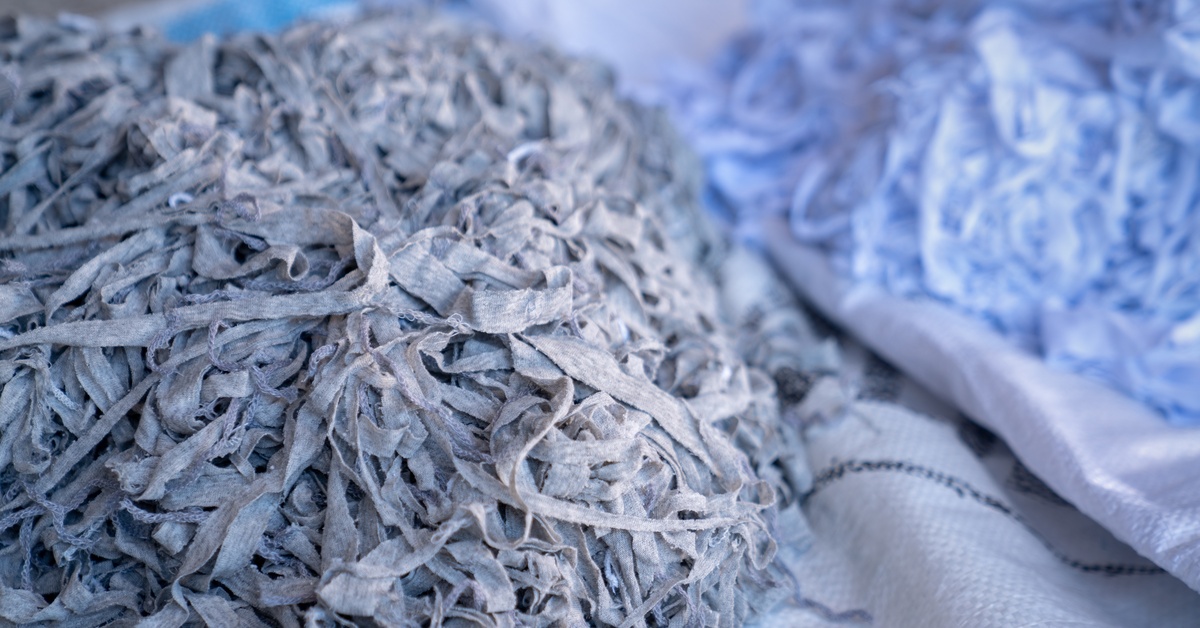 Long, messy strips of shredded gray fabric sitting in a large pile next to a second mass of shredded white fabric.