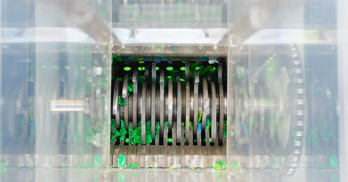 A shredder for plastic waste as viewed from the top of the shoot with the shredder's reflection on the shoot walls.