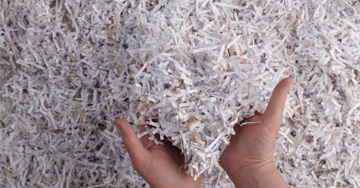 A person pushing their hands into a massive pile of white paper shreds and scooping some up toward the viewer.