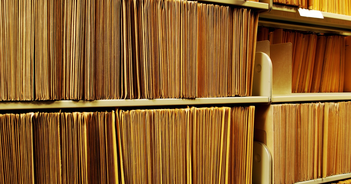 Rows of shelves packed to the brim with thin yellow file folders. There is only one empty shelf; the rest are full.