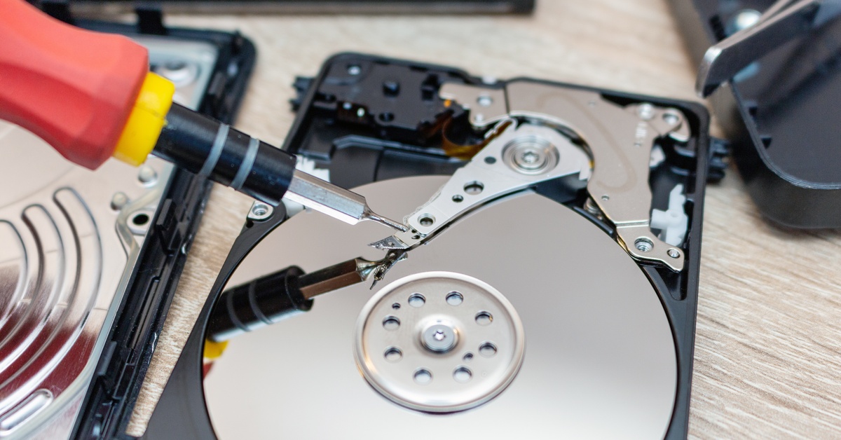 A person uses a recovery tool, reflecting on the disk drive, to repair and restore an old, black hard drive.