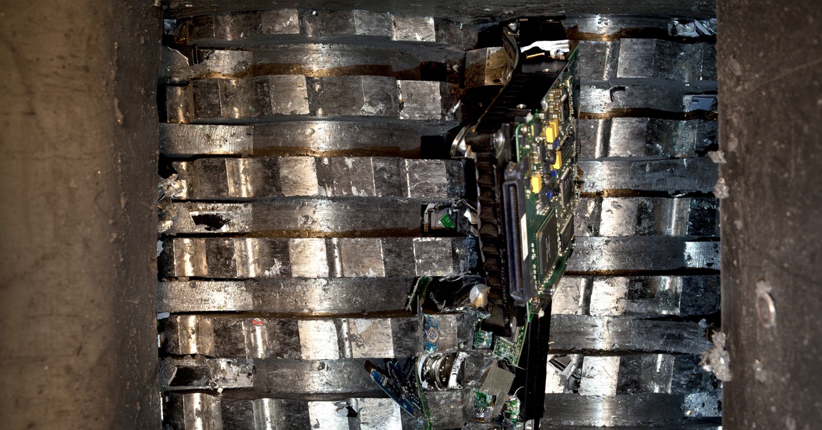 The light shines down on a silver, metallic shredder, showing a hard drive being destroyed in the shredder.