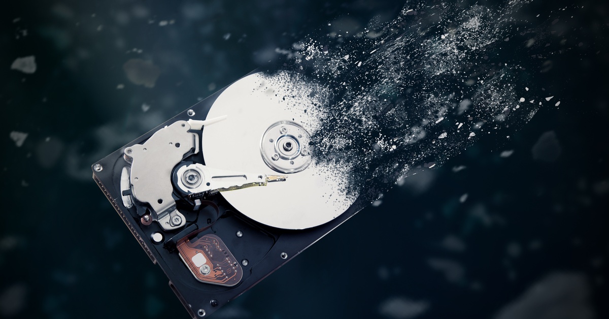 An old black-and-silver physical hard drive disintegrating into fine dust against a black background.