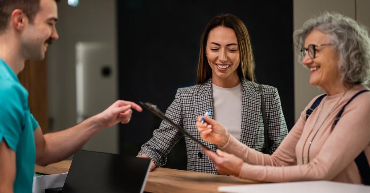 A patient handing over a clipboard with their personal information to a worker at a medical reception desk.