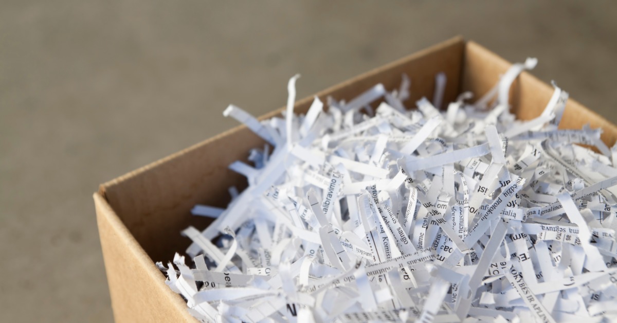 A small cardboard box briming with thin shreds of white paper with black text. The text is obscured by shredding.