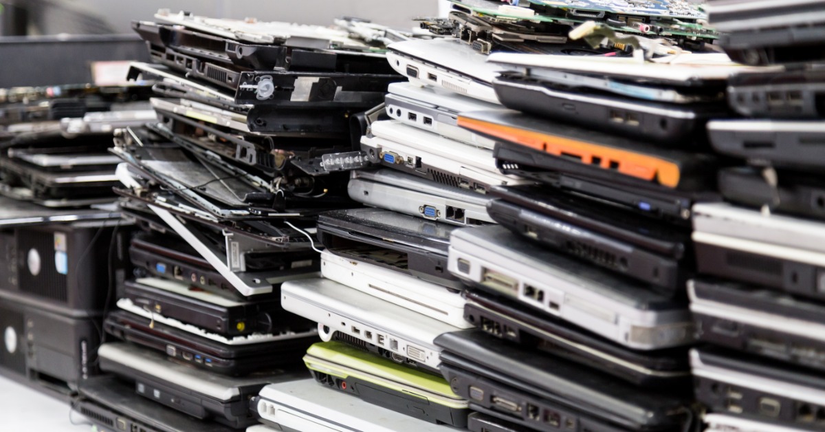 Stacks of closed laptops leaning against each other on a table. All of the laptops are in different states of disrepair.