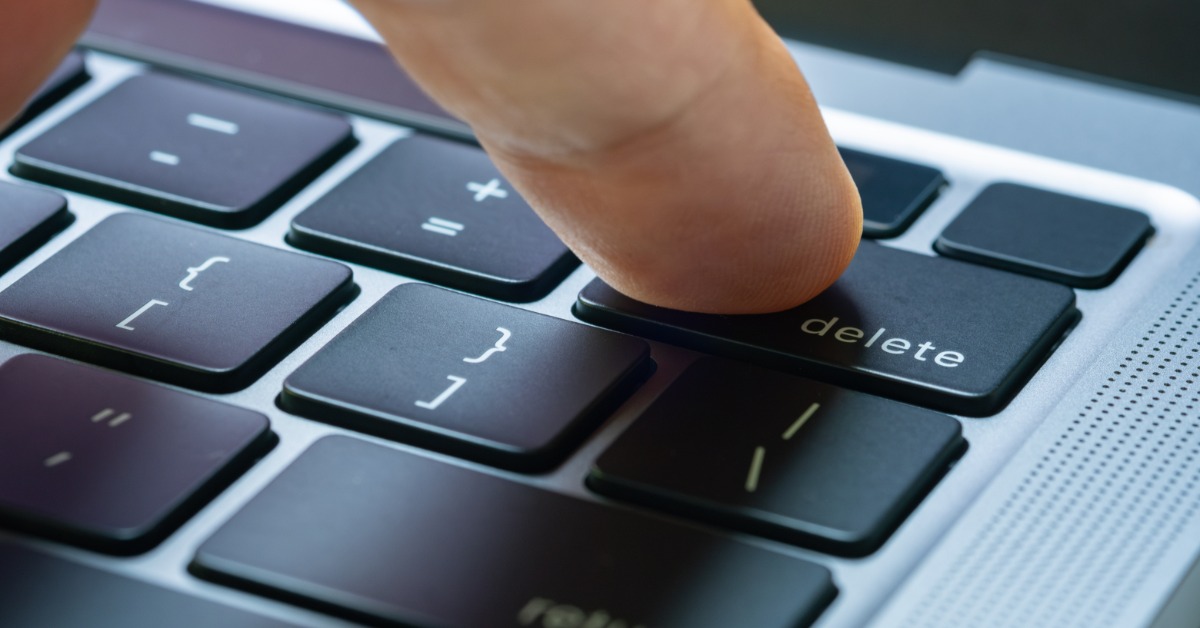 A person holding their finger over the "Delete" key on their laptop's keyboard. All of the keys are sleek and black.