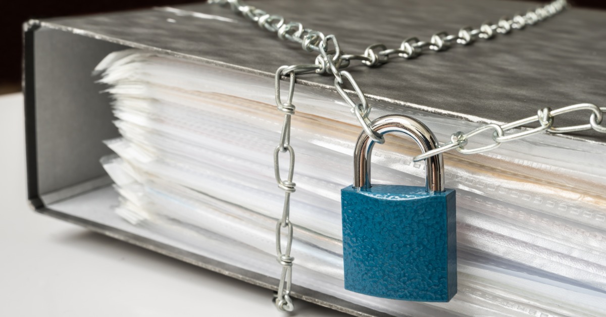A silver chain wraps around a binder holding a stack of papers in page protectors. A blue padlock fastens the chain.