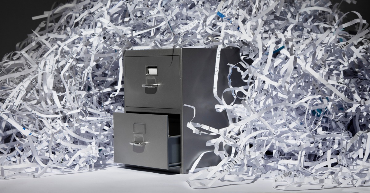 A spotlight shines on a pile of shredded white paper that towers over and around a gray, two-drawer filing cabinet.